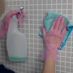 Ręce w różowych rękawiczkach czyszczą płytki. Zastanawiasz się, czym umyć fugi? Spray i ściereczka to dobry początek.