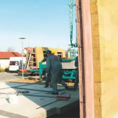 Budowa domu z keramzytu. Pracownicy montują prefabrykowaną ścianę na placu budowy.