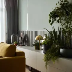 Musztardowe fotele i zielone rośliny ożywiają wnętrze. Jaki kolor pasuje do popielu? Złoto lampki i dekoracji dodaje elegancji.