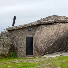 Niezwykły dom z kamienia, wbudowany w gigantyczne głazy, z dachem pokrytym dachówką i czarnymi drzwiami.