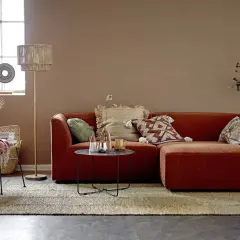 Przytulny salon w stylu boho. Pomarańczowa kanapa, wiklinowy fotel i dywan tworzą ciepłą paletę kolorów ziemi.