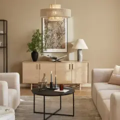 Jasny salon z beżową kanapą, drewnianą komodą i czarnym stolikiem kawowym.