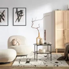 Przytulny salon w stylu hygge wnętrza. Jasne fotele, czarna skórzana kanapa, drewniana szafka z rattanowymi drzwiczkami i abstrakcyjne obrazy tworzą ciepłą atmosferę.