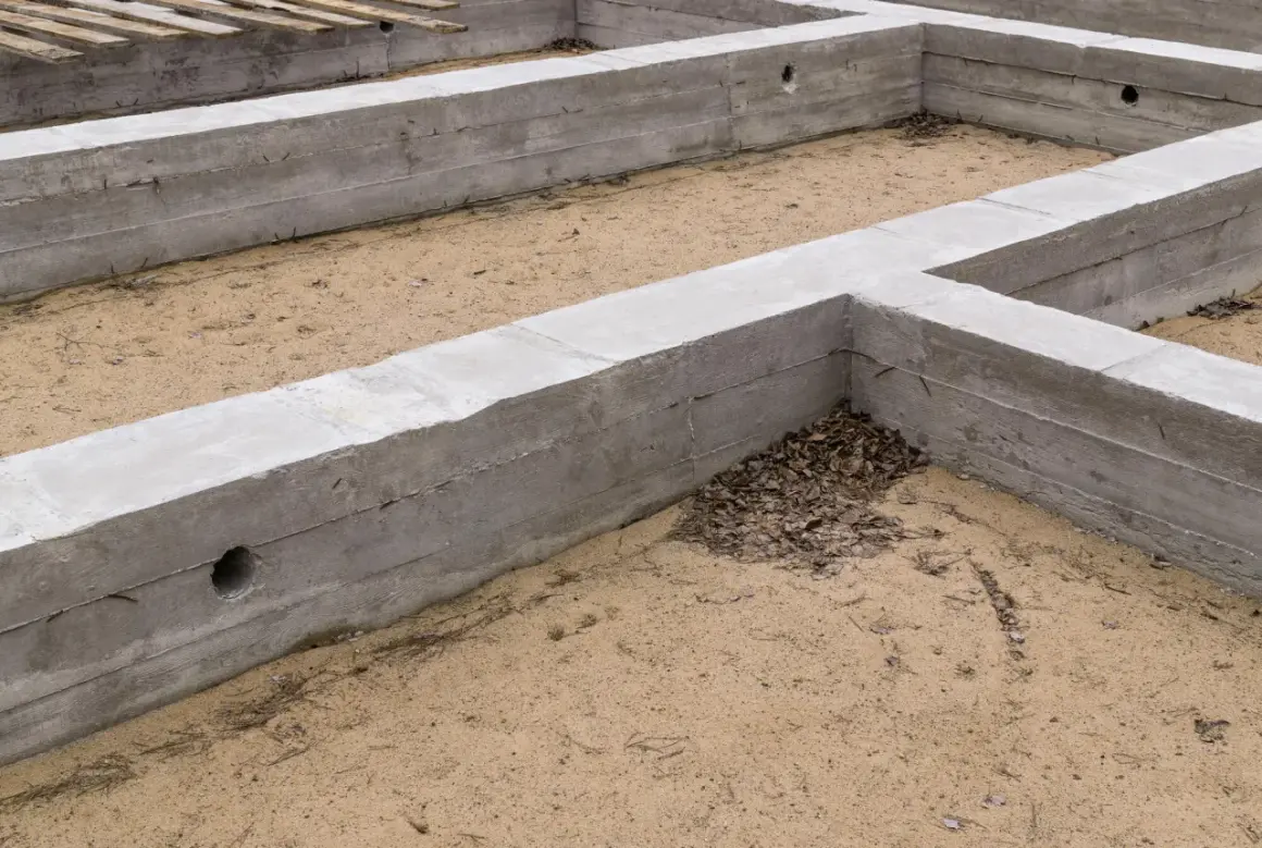 Betonowe fundamenty tworzą zarys przyszłego domu. To stan zero budynku, gdzie piasek miesza się z opadłymi liśćmi.